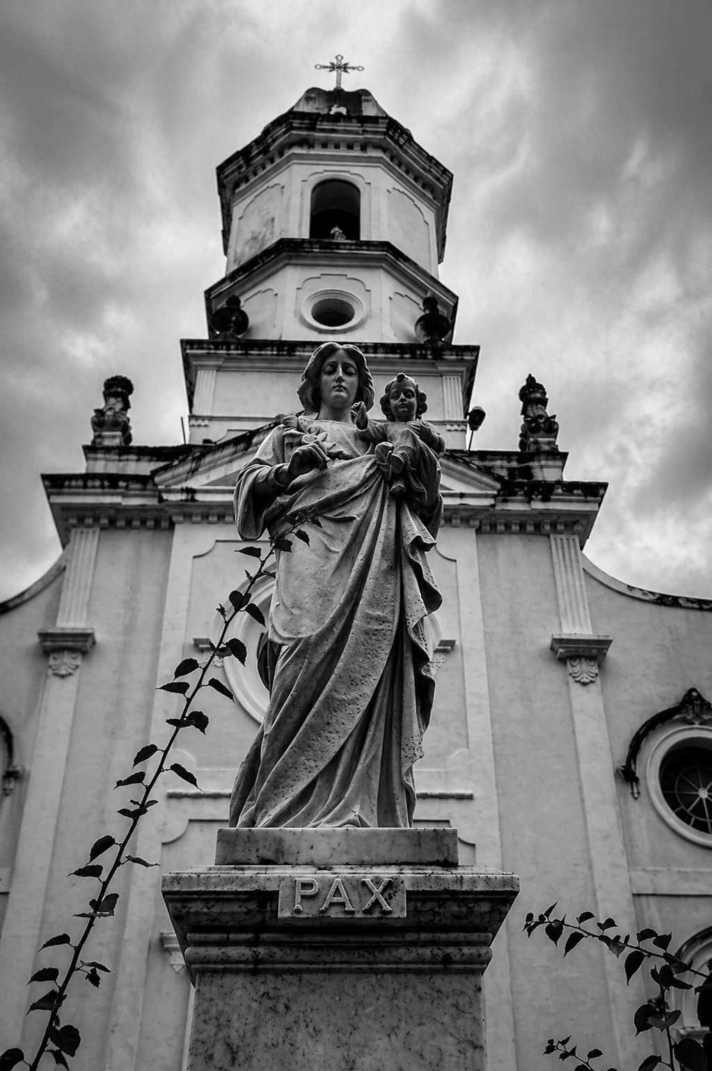 Estátua religiosa diante da torre de uma igreja em preto e branco