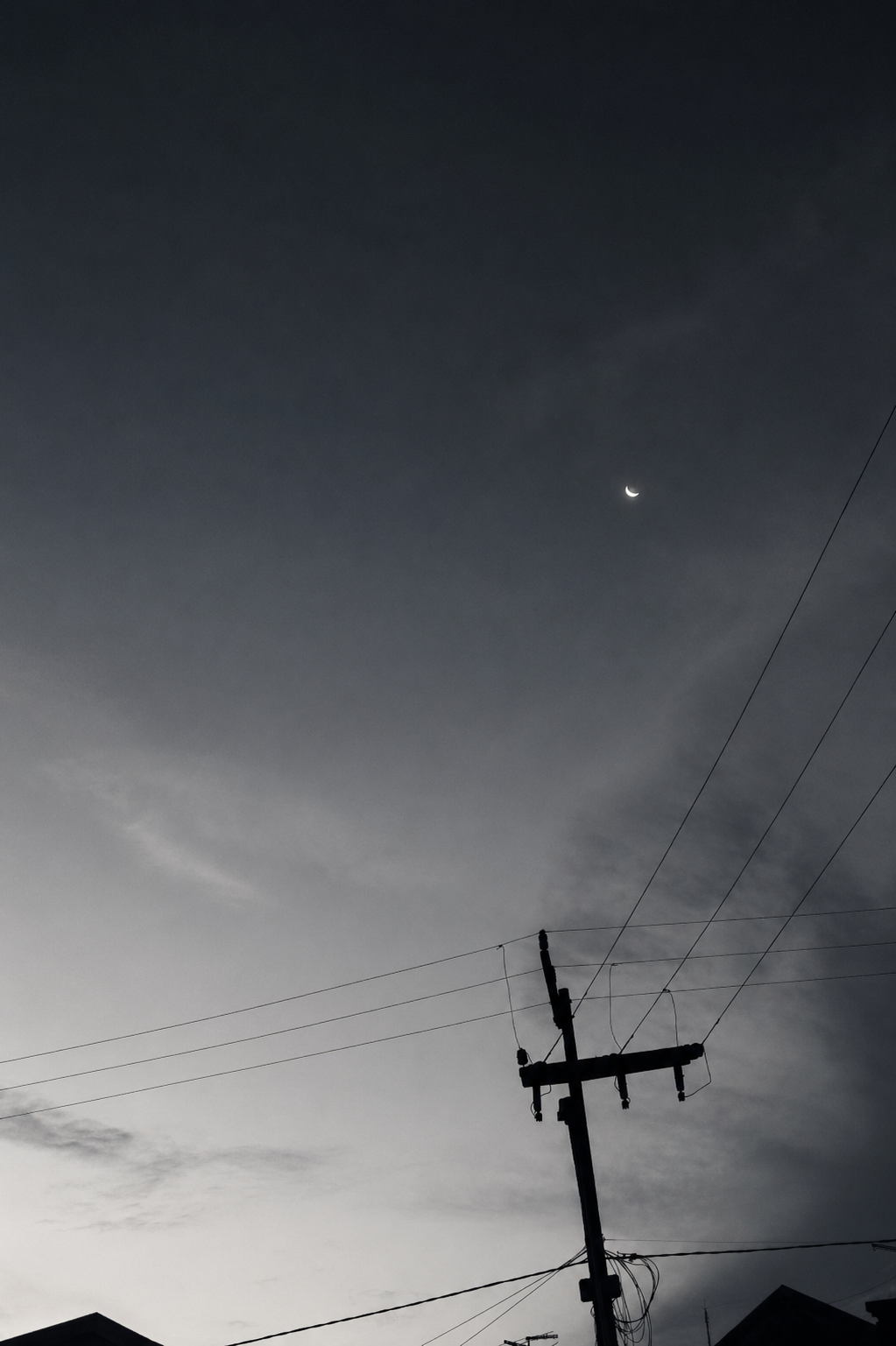Poste e fios em silhueta sob céu escuro com uma pequena lua crescente